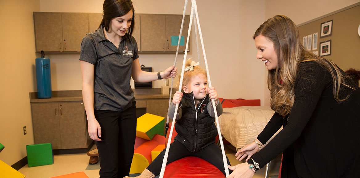 Students work with a toddler in one of the speech clinic rooms