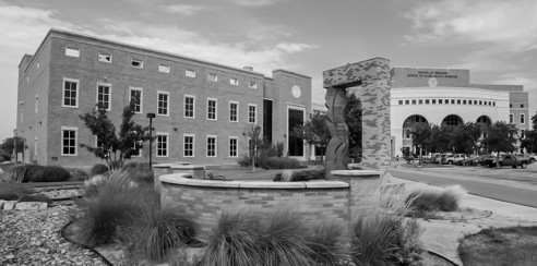 A modern university building with a central stone archway and landscaping.