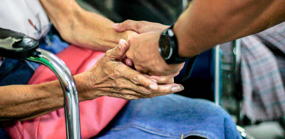 Image of a person holding hands with another person who is sitting in a wheel chair