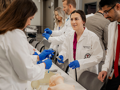 Medicine students around a dummy with blue gloves on smiling