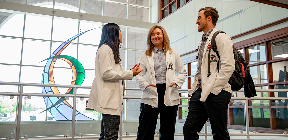 Amarillo SOM studets in white coats standing in the lobby smiling at each other 