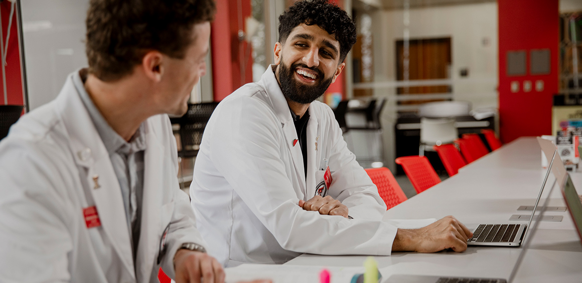 Two TTUHSC students sitting at a table in white lab coats smiling
