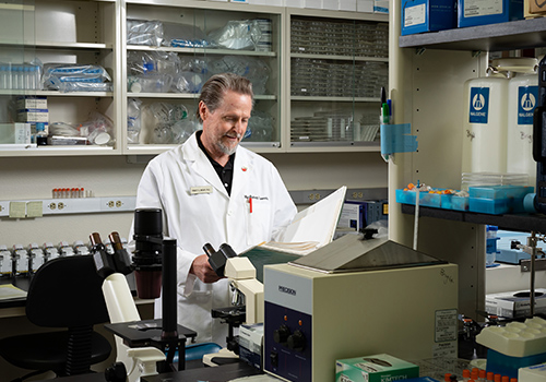man in white lab coat in a lab staring at paperwork smiling man in white lab coat in a lab staring at paperwork smiling