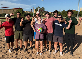 Students standing on a volleyball court smiling with the Texas Tech guns up with their hands