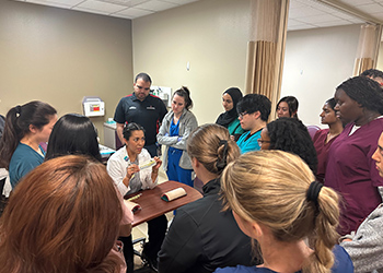 Students standing around a provider holding an object sitting at a table in patients room