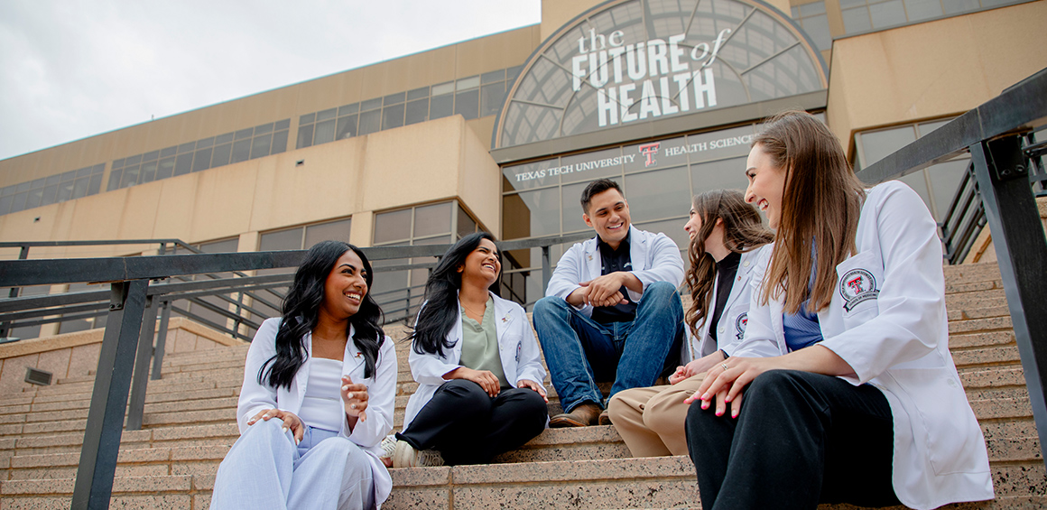 Group image of students in white lab coats sitting on steps of TTUHSC building in Lubbock