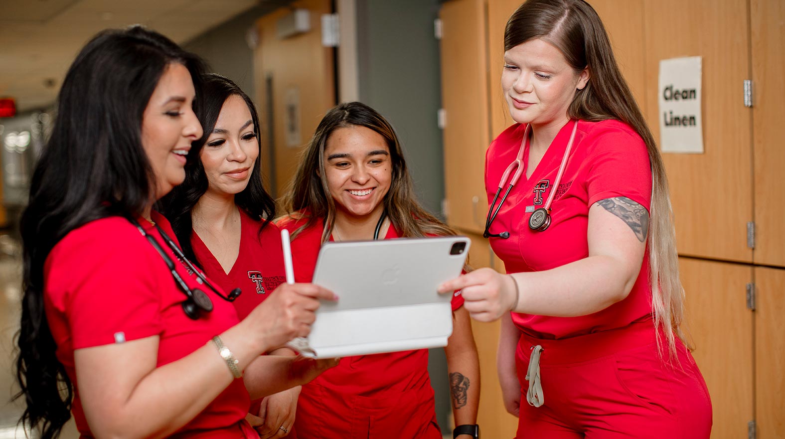 nursing students standing in a hall pointing to an ipad smiling