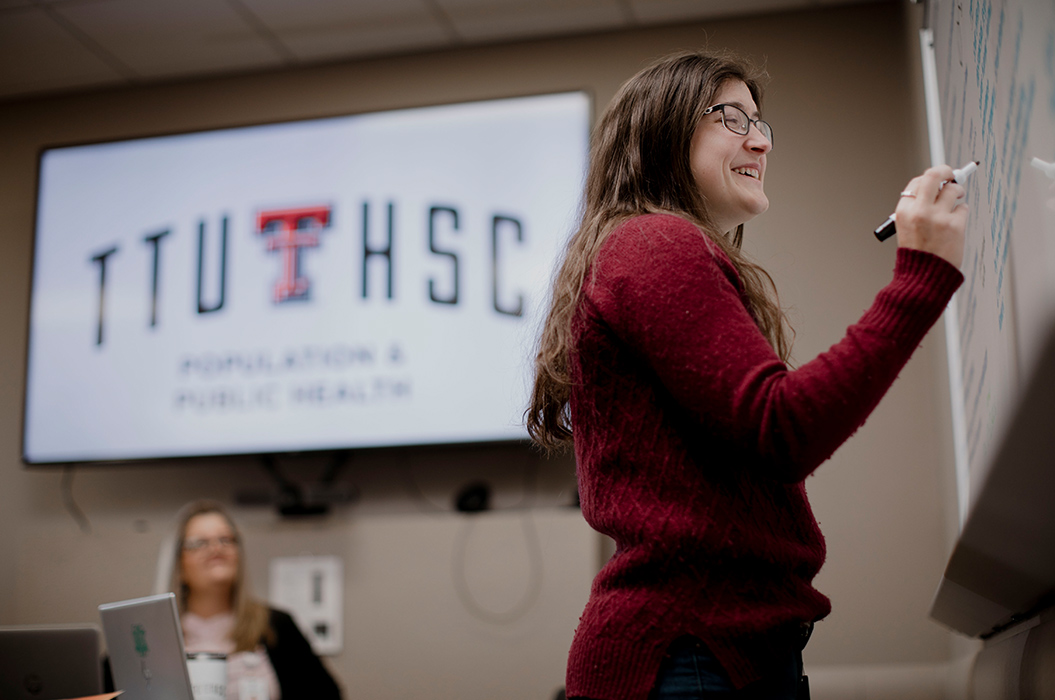public health student writing on a dry erase board smiling in a classroom